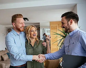 Couple shaking hands with a lender inside a home